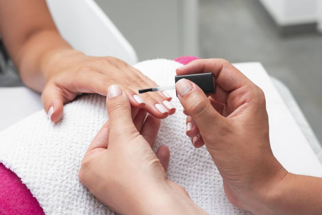 Professional nail technician applying nail polish during a manicure session in a clean and hygienic salon